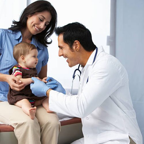 Doctor In Surgery Examining Baby Girl With Mother Smiling.