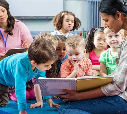 istockphoto-544351338-612x612 Female teacher giving a lesson to nursery students. They are sitting on the floor and there is a teacher taking notes.