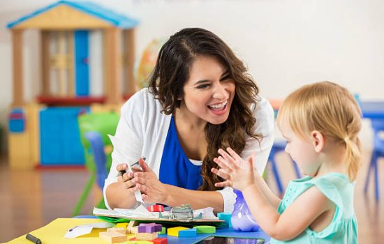 istockphoto-607460746-612x612 Cheerful female Hispanic teacher praises adorable blonde Caucasian little girl on accomplishing a project. The preschooler claps along with the teacher.